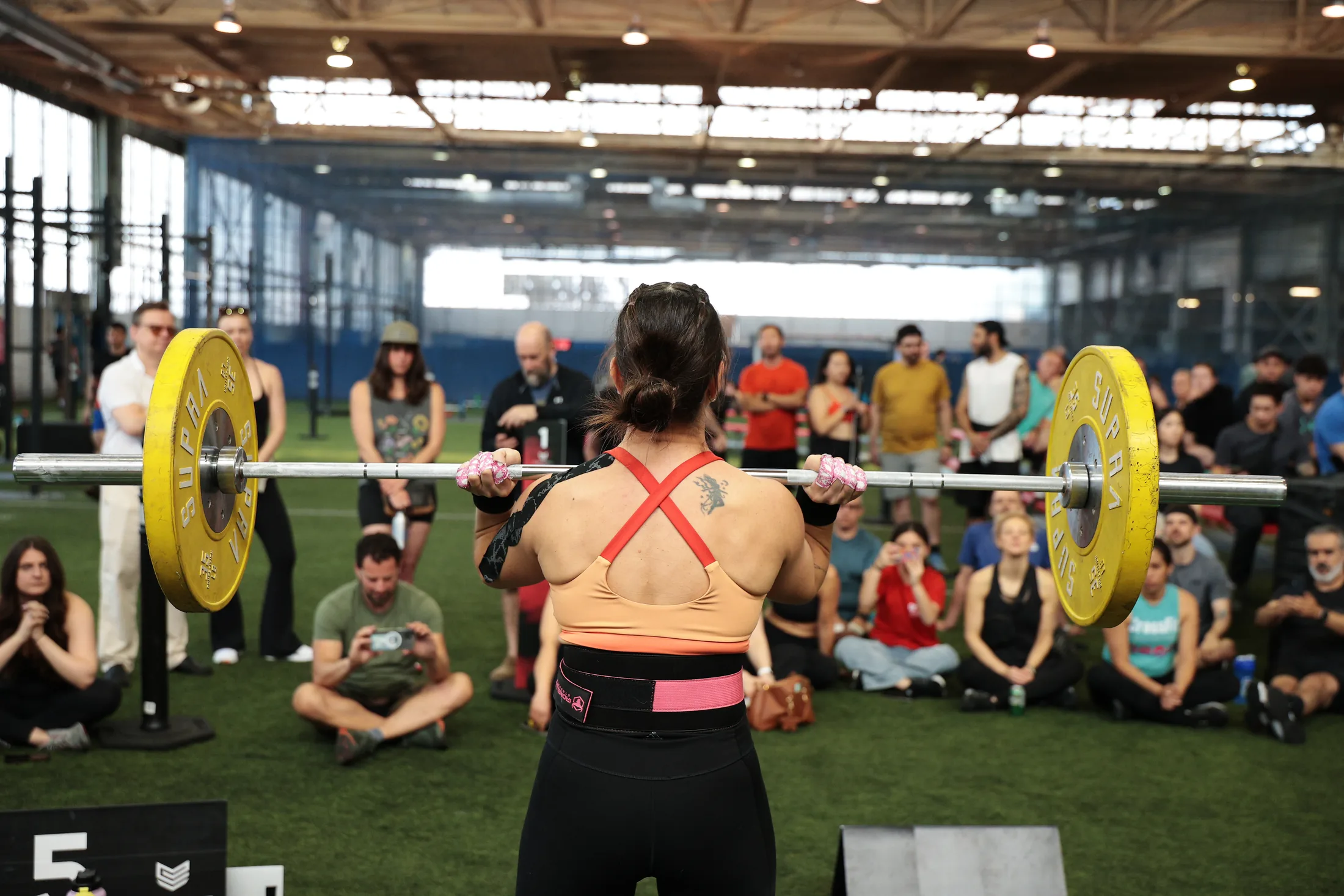 An athlete pressing a loaded barbell on the competition floor, crowd seated around